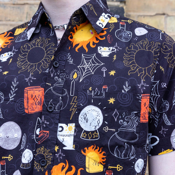 Close up of model wearing Run & Fly x Katie Abey Solar Witch Short Sleeve Shirt paired with blue jeans. The shirt is black with an all over print of Katie Abey witchy illustrations. The close up shows the print in more detail.