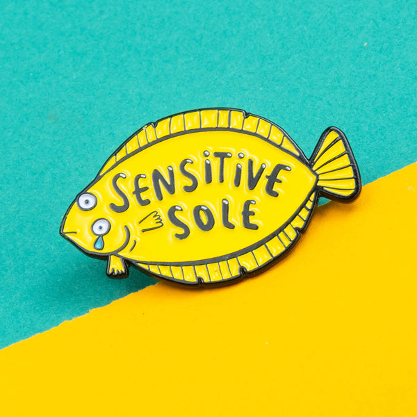 Sensitive Soul Soft Enamel Pin Badge designed by Katie Abey. It is a yellow fish crying with text say 'Sensitive Sole' on the pin it is on a green background