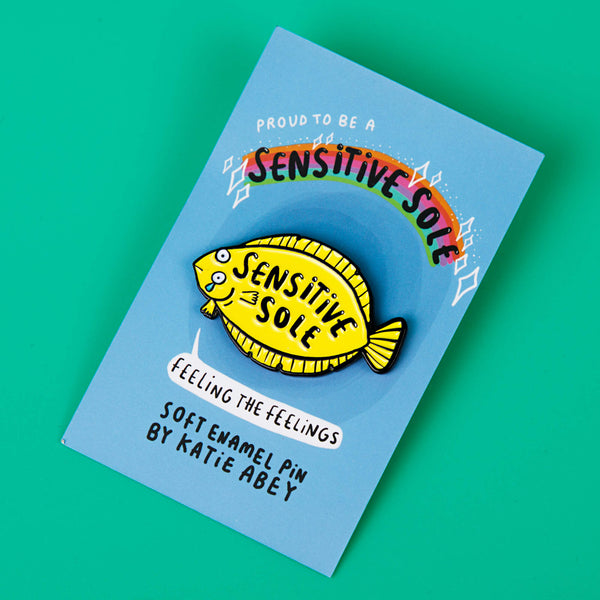 Sensitive Soul Soft Enamel Pin Badge designed by Katie Abey on a blue backing card. It is a yellow fish crying with text say 'Sensitive Sole' on the pin it is on a green background