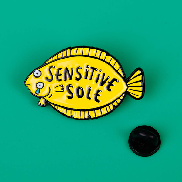 Sensitive Soul Soft Enamel Pin Badge designed by Katie Abey. It is a yellow fish crying with text say 'Sensitive Sole' on the pin it is on a green background