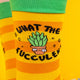 A close-up of the “What the Fucculent?” design on the socks, showing a quirky succulent in a pot with sassy lettering and small decorative stars on a sunny striped background.