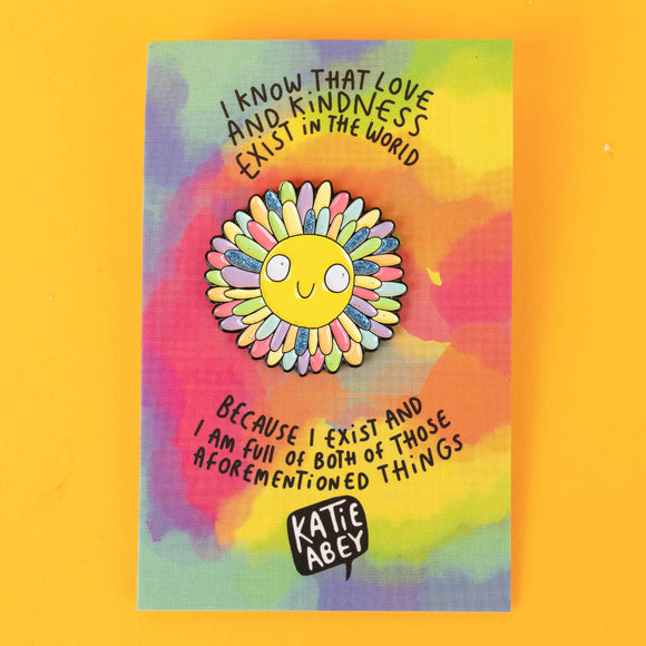 A colourful enamel pin from Katie Abey featuring a smiling sun with rainbow petal rays, mounted on a vibrant backing card with the quote: "I know that love and kindness exist in the world because I exist and I am full of both." Perfect for spreading positivity.