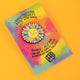 Katie Abey's enamel pin featuring a grinning sun surrounded by rainbow petal rays with glitter accents, displayed on a colourful backing card with an uplifting quote. A vibrant and whimsical accessory for weird and wonderful souls.