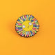 Katie Abey enamel pin showing a happy sun with rainbow and glitter rays. Bright and bold, this pin is a cheerful addition to bags, jackets, and pinboards, made to remind you of the love and kindness in the world.