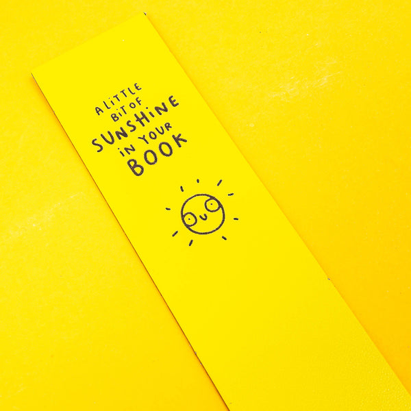 Yellow Leather Bookmark with black writing reads 'A little bit of sunshine in your book' with smiley illustrated sun. Designed by Katie Abey in the UK