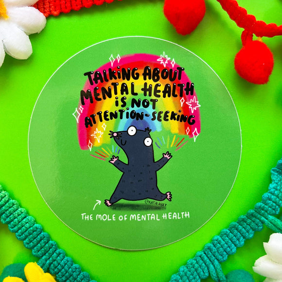  Green circular sticker of a mole with rainbows coming from its fingertips with text above saying talking about mental health is not attention seeking