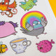 Detailed view of Katie Abey temporary tattoo sheet featuring a rainbow pigeon, grumpy pufferfish and patterned teacup character, showcasing bright colours and fun, expressive illustrations.
