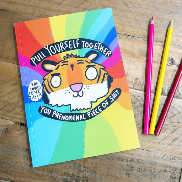 A notebook with a rainbow backdrop and an illustration by Katie Abey of a Tigers Head with Pull yourself together you phenomenal piece of shit, with a speech bubble saying The Tough Love Tiger