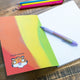 A notebook with a rainbow backdrop and an illustration by Katie Abey of a Tigers Head with Pull yourself together you phenomenal piece of shit, with a speech bubble saying The Tough Love Tiger laid open on a table