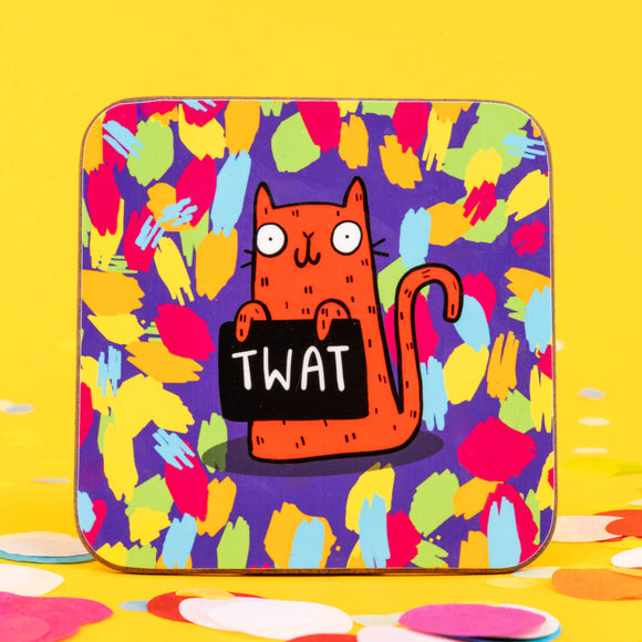 A coaster of an orange cat holding a sign saying 'TWAT' on a purple background with blue, green, pink and orange splats. The cat is smiling and looks very cheeky