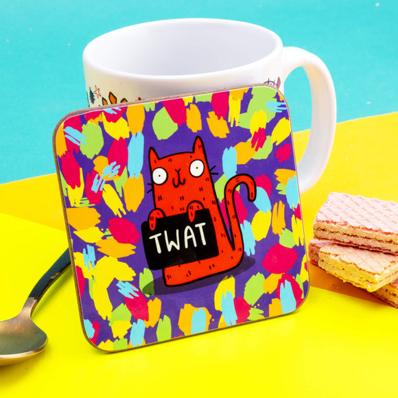 A coaster of an orange cat holding a sign saying 'TWAT' on a purple background with blue, green, pink and orange splats. The cat is smiling and looks very cheeky