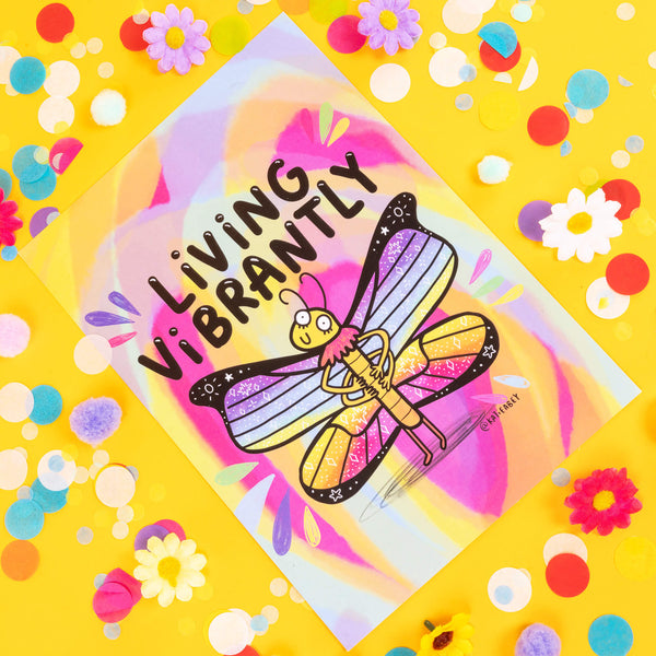 Butterfly Living Vibrantly A4 Print. An A4 size rainbow print with a rainbow winged butterfly illustration and black text that reads 'living vibrantly'. Print is shown in front of yellow background with confetti and flowers of various bright colours