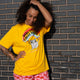 Person posing in the Katie Abey Woke Up and Chose Violence Hamster Adults Tee in Spectra Yellow. The yellow unisex t shirt features a colourful hamster illustration holding chainsaws with a rainbow slogan. Designed by UK illustrator Katie Abey, this quirky adult tee is ideal for bold, playful and alternative wardrobes.
