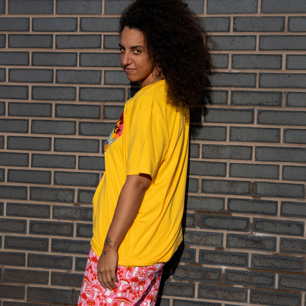 Side view of a person wearing the Katie Abey Woke Up and Chose Violence Hamster Adults Tee in Spectra Yellow. The oversized yellow t shirt shows a relaxed fit and is styled with pink patterned trousers. Fun, quirky illustrated slogan tee by Katie Abey, a UK small business celebrating weird and joyful self expression.
