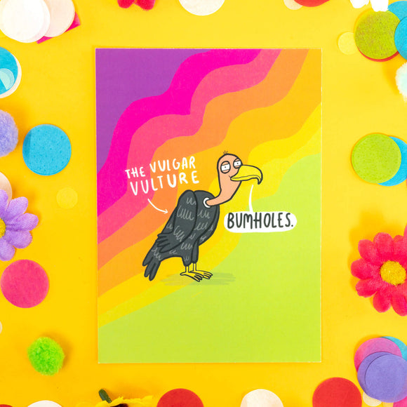 a postcard of an illustration drawn by Katie Abey of the Vulgar Vulture saying Bumholes against a rainbow wavy background. It is laid on a yellow backdrop with confetti, fake daisies and pom poms of various colours
