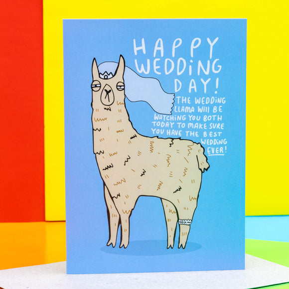 Happy Wedding day a6 greeting card. The front cover is a blue background with a beige llama illustration wearing a white crown, veil and garter looking forward. Around the llama reads 'Happy Wedding Day! The wedding llama will be watching you both today to make sure you have the best wedding ever!' Designed by Katie Abey in the UK.