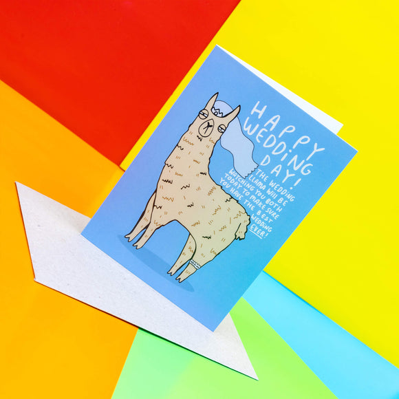  Happy Wedding day a6 greeting card. The front cover is a blue background with a beige llama illustration wearing a white crown, veil and garter looking forward. Around the llama reads 'Happy Wedding Day! The wedding llama will be watching you both today to make sure you have the best wedding ever!' Designed by Katie Abey in the UK.