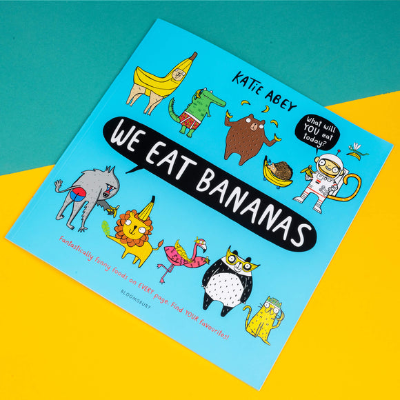 We Eat Bananas book by Katie Abey. The cover is a light blue with various animals wearing or holding bananas with text in the middle reading 'we eat bananas'. One animal has a speech bubble reading 'what will YOU eat today' and bottom text reads 'fantastically funny foods on EVERY page. Find YOUR favourites!' Printed by Bloomsbury.