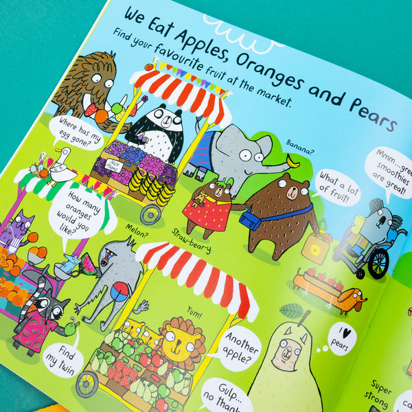 We Eat Bananas book by Katie Abey laying open flat on . The brightly coloured page spread features various animals at a market discussing various foods. 
