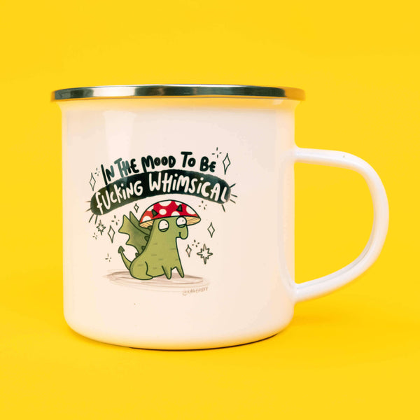 Katie Abey In the mood to be f***ing whimsical enamel mug with a white body and silver rim, featuring a whimsical hand drawn illustration of a green creature with a red and white mushroom cap. Above the illustration is the humorous phrase 'In The Mood To Be Fucking Whimsical' in bold black and white lettering. The mug is set against a bright yellow background