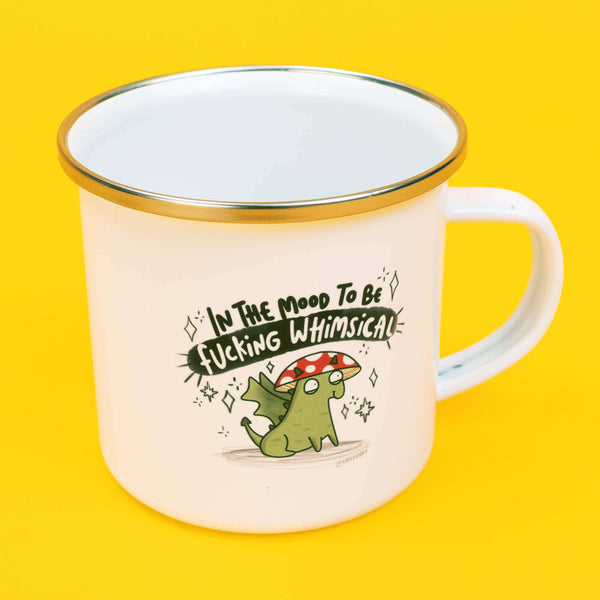 Katie Abey In the mood to be f***ing whimsical enamel mug with a white body and silver rim, featuring a whimsical hand drawn illustration of a green creature with a red and white mushroom cap. Above the illustration is the humorous phrase 'In The Mood To Be Fucking Whimsical' in bold black and white lettering. The mug is set against a bright yellow background