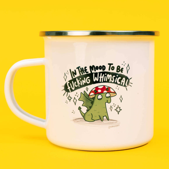 Katie Abey In the mood to be f***ing whimsical enamel mug with a white body and silver rim, featuring a whimsical hand drawn illustration of a green creature with a red and white mushroom cap. Above the illustration is the humorous phrase 'In The Mood To Be Fucking Whimsical' in bold black and white lettering. The mug is set against a bright yellow background