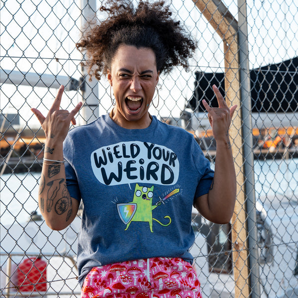 Model posing playfully in the Wield Your Weird Adults Tee in dark heather blue by Katie Abey. The illustrated cat graphic and slogan are shown clearly on the front of the tee. A colourful graphic t shirt by an independent illustrator celebrating individuality and embracing your weird side.
