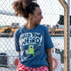 Three quarter view of a model wearing the Wield Your Weird Adults Tee in dark heather blue by Katie Abey. The playful slogan and illustrated cat design are clearly visible, styled casually outdoors. A comfortable adults graphic t shirt with a relaxed fit and positive message.
