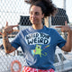 Front view of a model wearing the Wield Your Weird Adults Tee in dark heather blue by Katie Abey. The model points at the slogan on the t shirt, clearly showing the fun illustrated cat character and bold lettering. A joyful unisex graphic tee designed to celebrate being weird.
