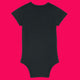 Black organic cotton babygrow shown from the back on a bright pink background. Plain black baby bodysuit with short sleeves, ribbed neckline and leg openings, and snap fastening at the bottom. A comfy unisex babygrow designed for everyday baby wear.