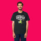 Front view of a model wearing the Wield Your Weird Adults T Shirt by Katie Abey in black. The playful illustrated slogan design is clearly visible on the chest, styled with dark trousers on a bright pink background.