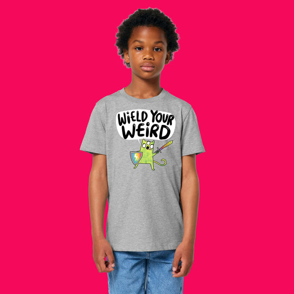 Child wearing heather grey Wield Your Weird kids t shirt by Katie Abey, featuring colourful cartoon artwork and bold text. Soft organic cotton unisex children’s tee with a comfy fit, photographed on a bright pink background. Fun kids clothing celebrating creativity and individuality.
