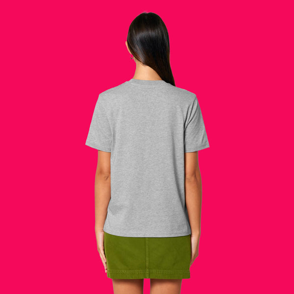 Back view of a model wearing the Wield Your Weird Adults T Shirt by Katie Abey in heather grey. The unisex fit T shirt is shown from behind on a bright pink background, paired with a green skirt for a casual everyday look.