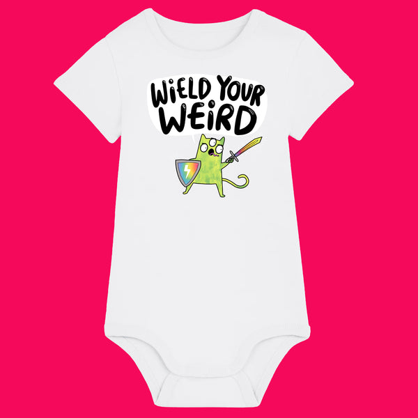 White organic cotton babygrow featuring Wield Your Weird artwork by Katie Abey. The front shows a cute green cat holding a sword and shield with the slogan “Wield Your Weird” above. Short sleeves, shoulder snap fastening and bottom poppers, photographed on a bright pink background.