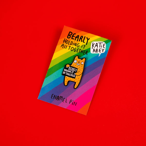 Bearly Holding it All Together soft enamel pin badge in shape of smiley yellow bear with black rubber clasp.Designed by Katie Abey in the UK.