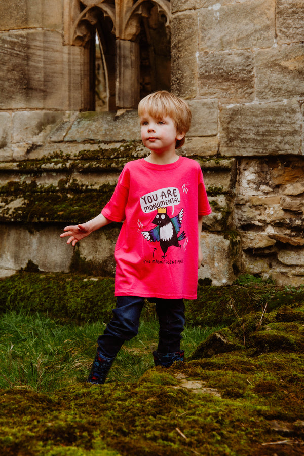 Monumental Magpie Pink Kids Tshirt 100% cotton tshirt with illustrated happy magpie design wearing crown with speech bubble and black writing that reads 'The Magnificent Magpie'. Designed in the UK by Katie Abey