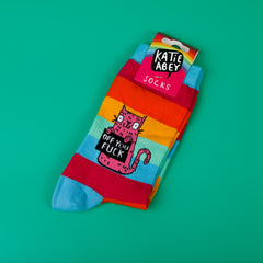 Pack of nine sweary cat socks with cat design on rainbow knitted pattern. 76% cotton, 22% polymide, 2% elastane. Pink cat holding sign on striped pattern. Designed by Katie Abey in the UK