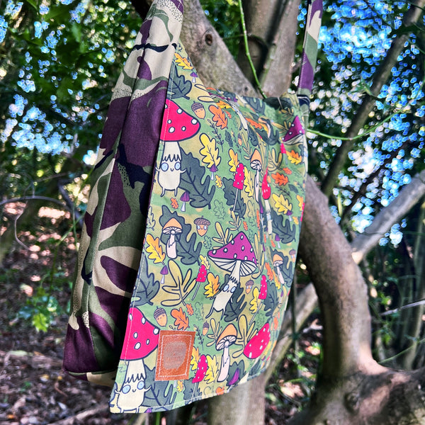 Mushroom Bois shoulder bag with green forest illustration featuring smiley mushrooms and acorns, lined with camouflage print fabric and strap. Designed by Katie Abey X Dawney's Sewing Room in the UK