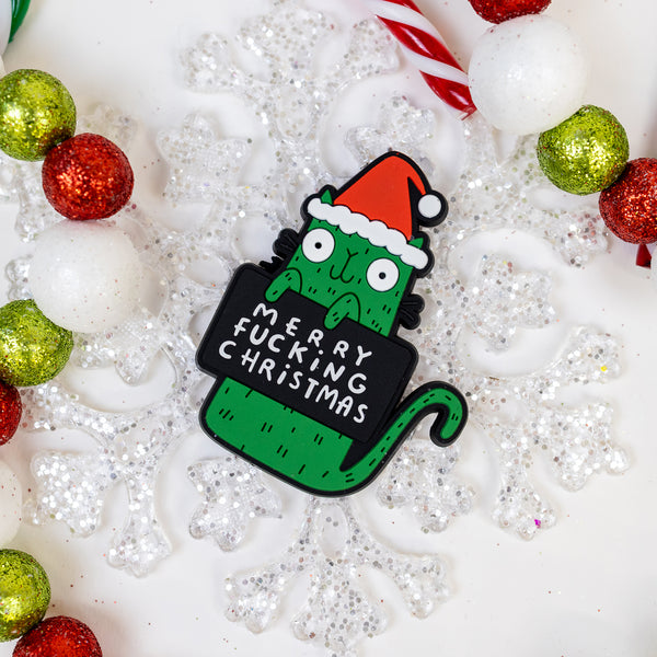 Merry Swear Word green cat fridge magnet holding funny sign and wearing red Santa hat. Designed in the UK by Katie Abey 