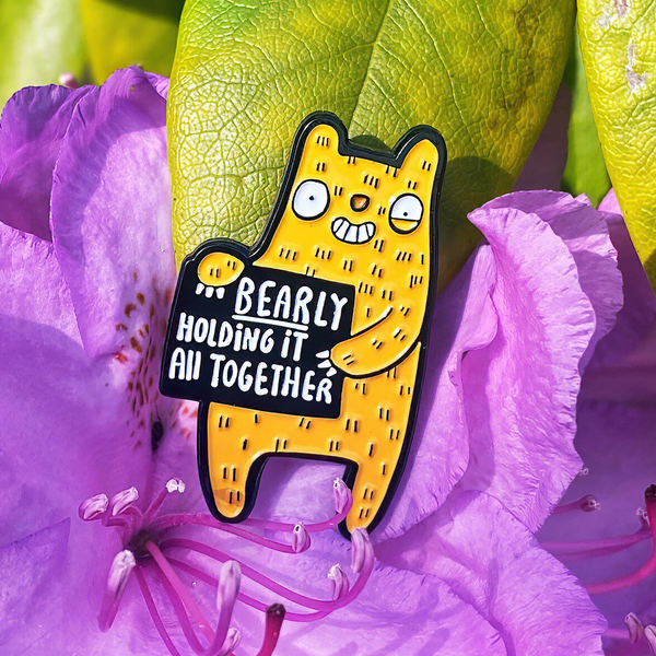 Bearly Holding it All Together soft enamel pin badge in shape of smiley yellow bear with black rubber clasp. Designed by Katie Abey in the UK