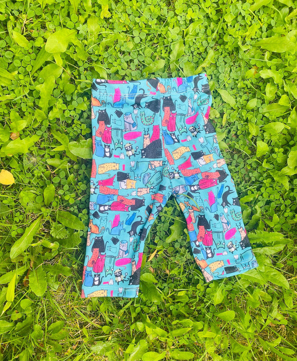 All of the cats baby leggings 0 - 3 months old size. The leggings are laying flat on a grassy area. The legging print are a blue base with various repeating cats in different colours, patterns and sizes. Designed by Katie Abey in the UK.