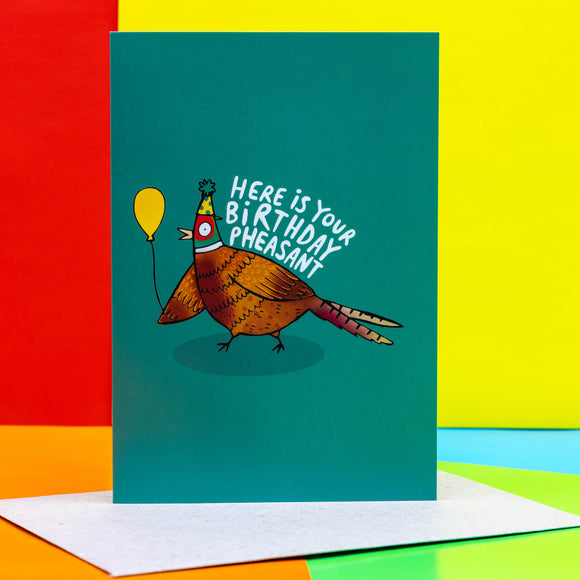 Fun happy birthday card featuring pheasant design holding a yellow balloon on a teal background. Designed by Katie Abey in the UK.